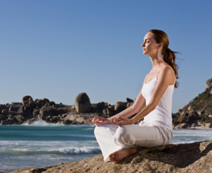 Beautiful young lady meditating on rock by sea