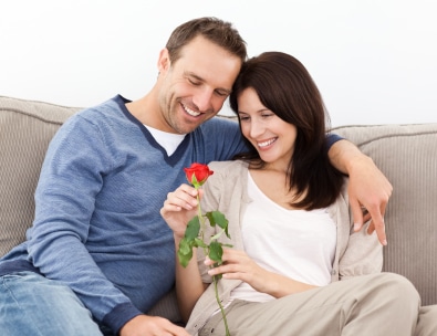 Portrait of a lovely couple looking at a red rose sitting on the sofa